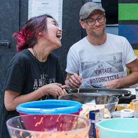 Junge Freiwillige der Tafel kochen zusammen und lachen.