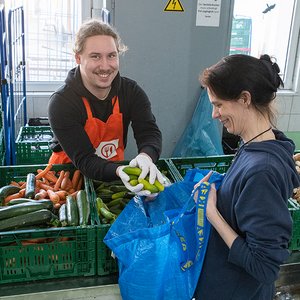 Ein ehrenamtlicher Helfer der Tafel Jugend überreicht einer Kundin Gurken.